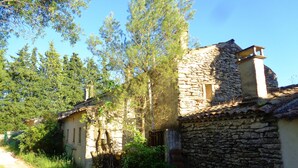 Ein rustikales Steinhaus mit traditionellem Ziegeldach, umgeben von viel Grün und einem Feldweg.