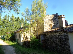 Un edificio rustico in pietra con tetto in tegole tradizionali, immerso nel verde e con un sentiero sterrato.