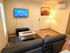 A living room with a sofa, a coffee table, a TV mounted on the wall, and an air conditioner.
