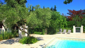 Ein Schwimmbecken, umgeben von Bäumen, mit einer Terrassenanlage und Liegestühlen.