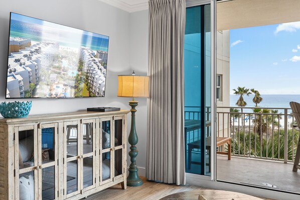 Un balcón con vista al océano, un televisor montado en la pared y un mueble con puertas de vidrio.