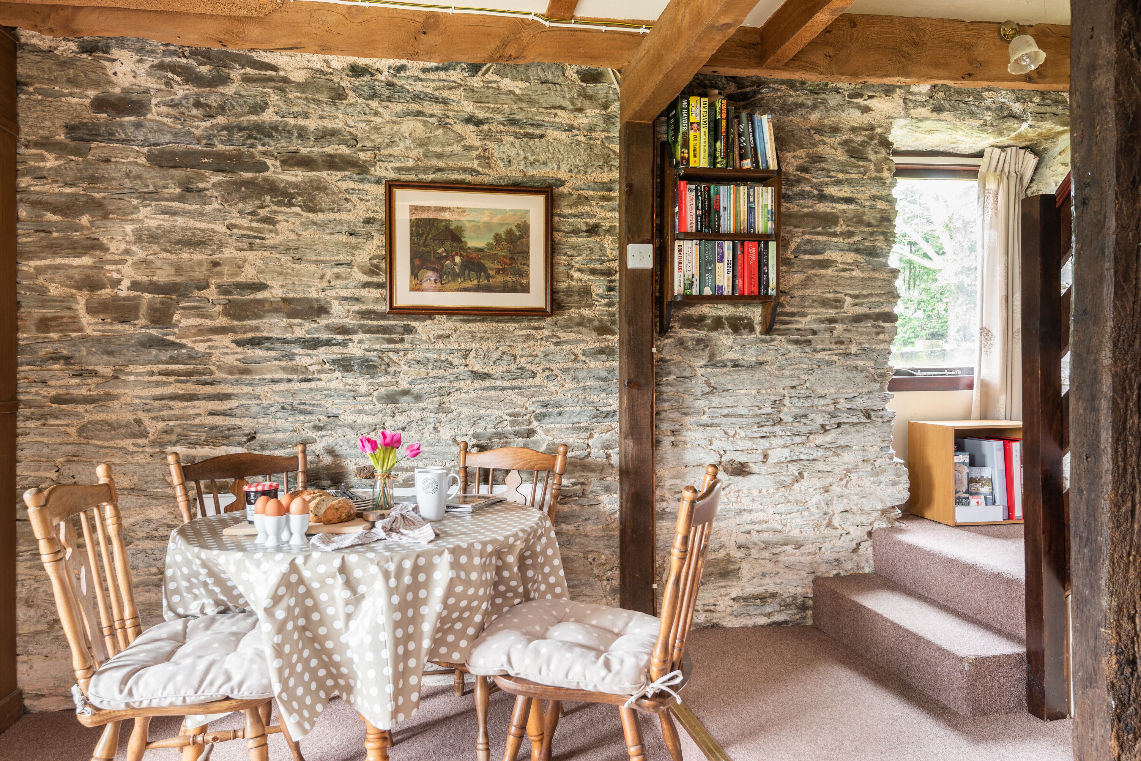 A rustic dining area with a stone wall, wooden furniture, a bookshelf, and a painting.