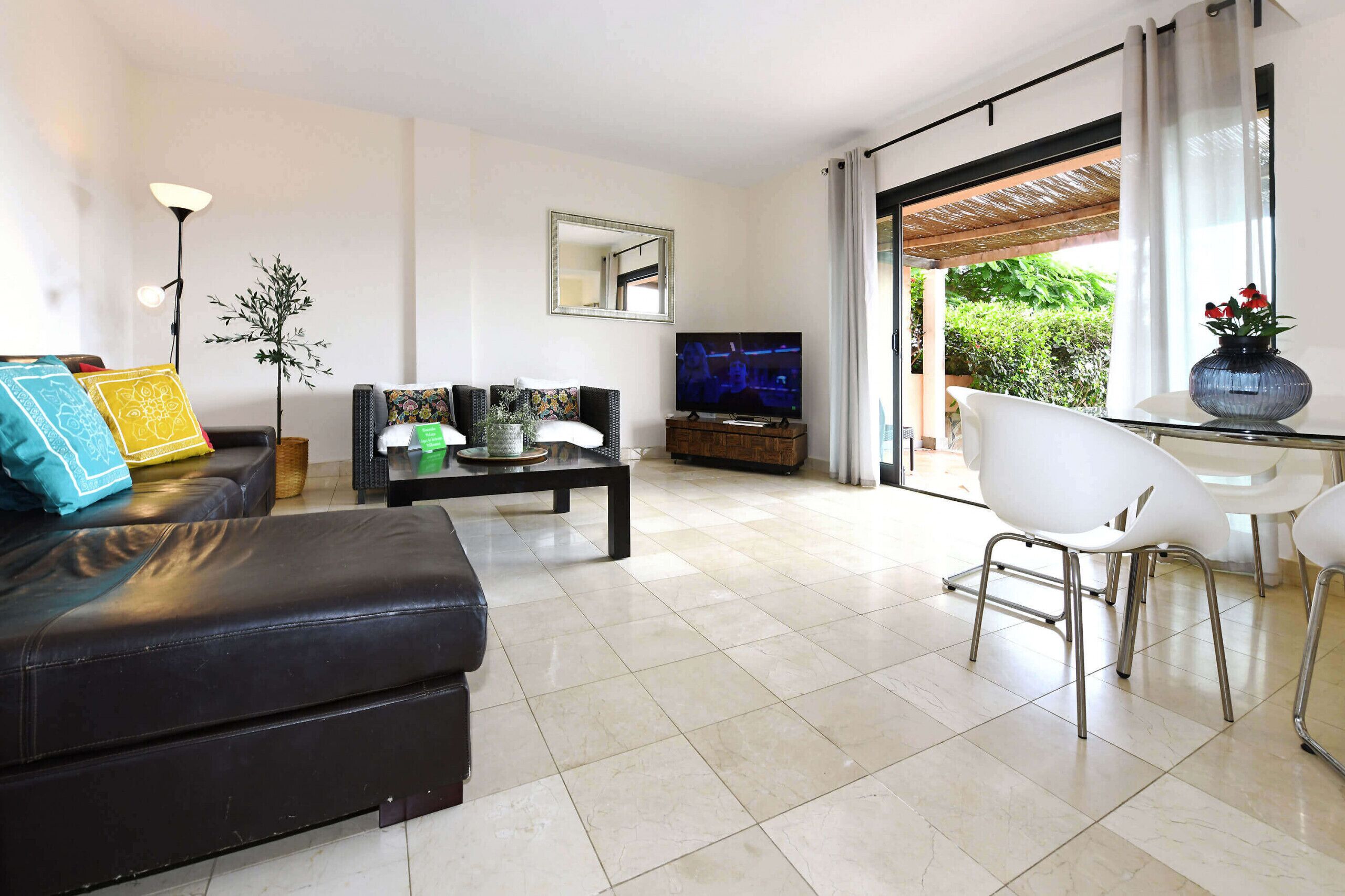Un salon moderne avec un canapé en cuir noir, une table basse, un téléviseur et un coin repas avec des chaises blanches.