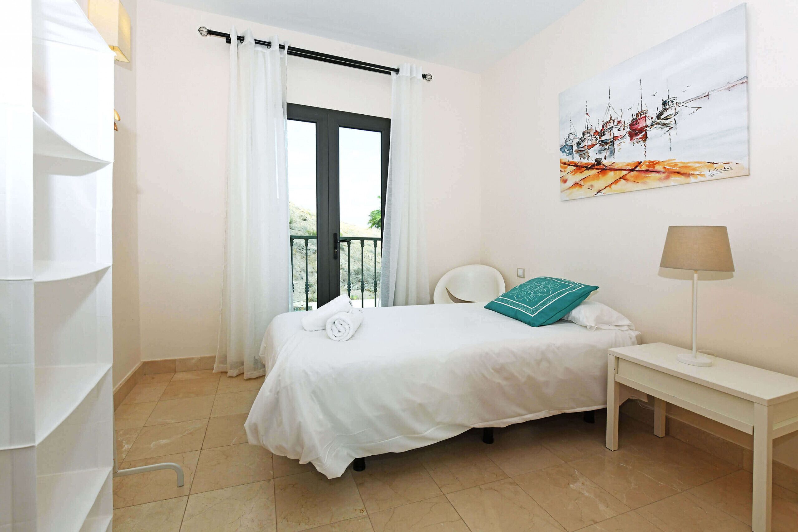 A hotel room with a bed, a bedside table, a lamp, a painting on the wall, and a window with curtains.