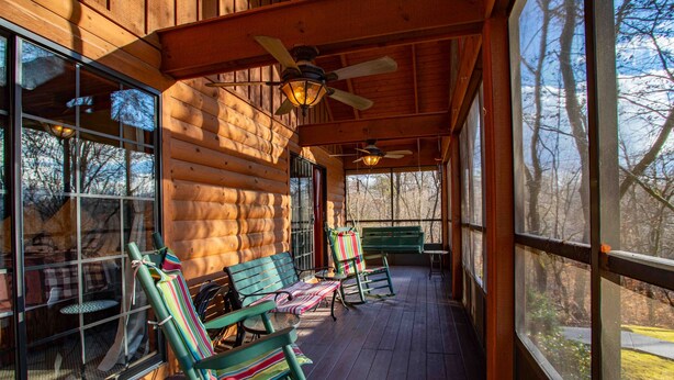 A log cabin with a porch, wooden walls, and large windows.