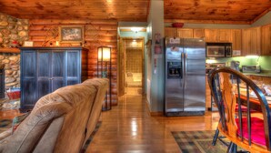 A wooden cabin interior with a kitchen, dining area, and a stone wall.