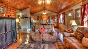 A cozy cabin interior with wooden ceilings and walls, a dining area, and a fireplace.