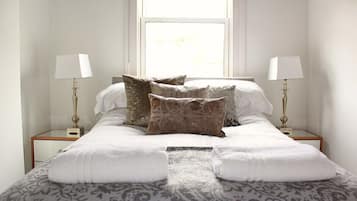 A neatly made bed with white linens and patterned pillows, two bedside lamps, and a window with a view.