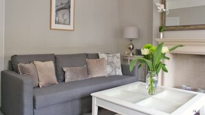 A living room with a grey sofa, a white coffee table, a framed picture on the wall, a lamp, and a vase with flowers. - Lovely Central Bath House- w/ Parking (CG) (Bath)