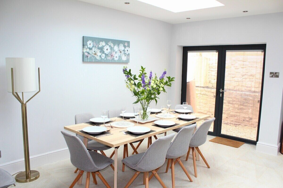 A dining area with a table set for six, a floor lamp, and a door leading to an outdoor area.