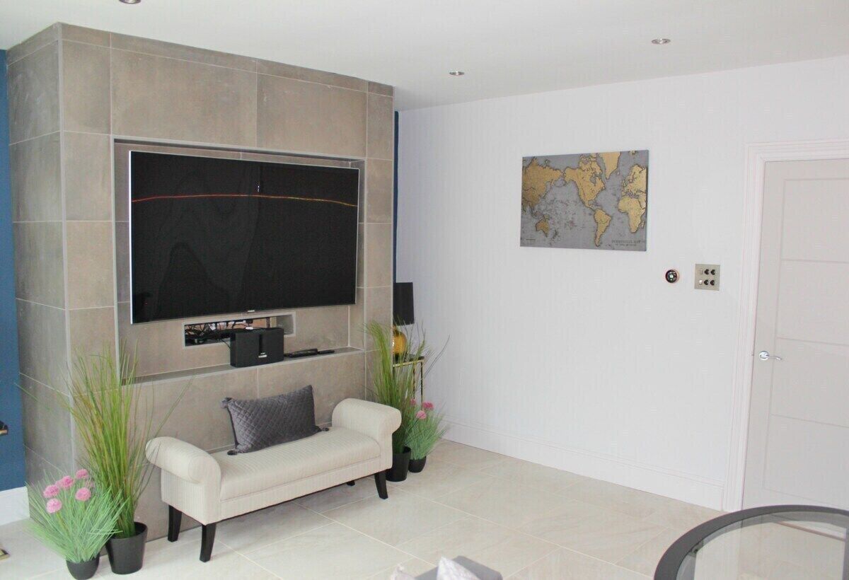 A living room with a flat-screen TV mounted on a wall, a sofa, and two potted plants.