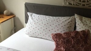 A bed with white bedding and a floral pattern, a decorative headboard, and a small wooden nightstand with a decorative item.