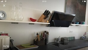 A modern kitchen with a black induction cooktop, a white shelf with glassware, a red bowl, and a knife block.