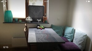 A cozy room with a dining table, a window with a view, a radiator, and a shelf with decorative items.