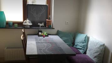 Ein gemütliches Zimmer mit Esstisch, Fenster mit Aussicht, Heizkörper und einer Regal mit Dekoration.