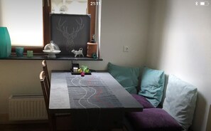 A cozy room with a dining table, a window with a view, a radiator, and a shelf with decorative items.