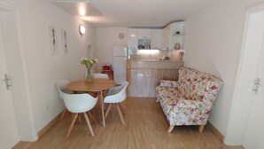 A compact living space with a dining area featuring a wooden table and white chairs, a floral-patterned sofa, and a kitchen with white cabinets and a built-in oven. - Holiday Home in Bol with Seaview, Terrace, Air condition, WIFI (120-1) (Bol)