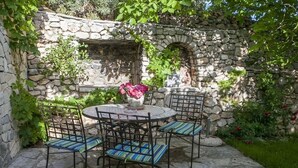 A stone patio with a round table and four chairs, surrounded by greenery and a stone wall. - Holiday Home in Bol with Seaview, Terrace, Air condition, WIFI (120-1) (Bol)