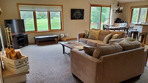A living room with a large sofa, a television, and a dining area with a table and chairs. - The Sixth Green at Lake Arrowhead by Sand Valley Golf Resort (Nekoosa)