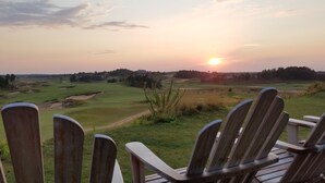 A view of a golf course at sunset with wooden chairs in the foreground. - The Sixth Green at Lake Arrowhead by Sand Valley Golf Resort (Nekoosa)