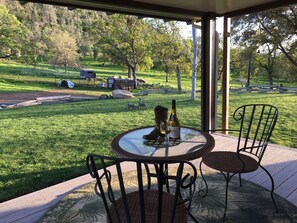 Un espace extérieur abrité, avec une table et des chaises, donnant sur un paysage verdoyant parsemé d’arbres et comprenant un petit bâtiment.