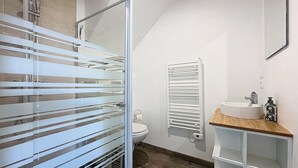 Une salle de bain avec une douche à parois de verre, des toilettes, un porte-serviettes, un radiateur et un meuble-lavabo en bois avec un évier.