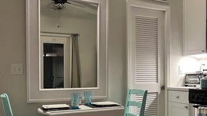 A dining area with a white table and turquoise chairs, a large mirror, and a kitchen with a stove and oven. - 1 Bedroom Suite in a duplex house- private heated pool for you- walk to beach  (Lauderdale-By-The-Sea)