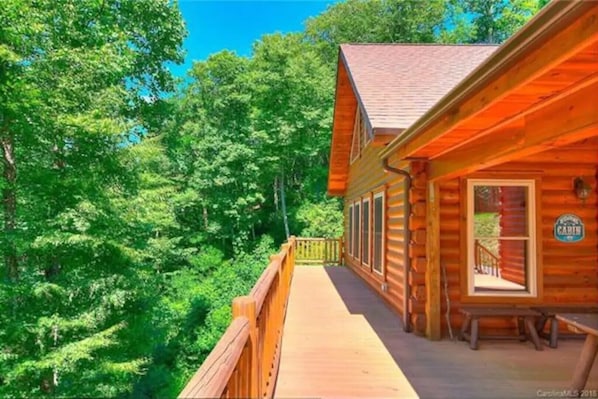 Una cabaña de madera con terraza, rodeada de un bosque frondoso.