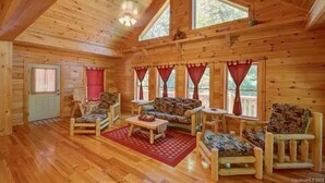 A log cabin interior with a high ceiling, wooden walls, a sofa set, and a dining table.