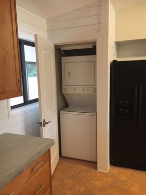 Een compacte keuken met een ingebouwde wasmachine en droger, houten kastjes en een zwarte koelkast.