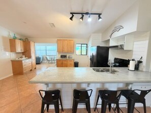 A modern kitchen with a central island, bar stools, and a dining area with a window.