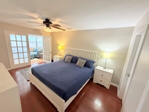A bedroom with a bed, nightstands, a ceiling fan, and a view through a glass door.