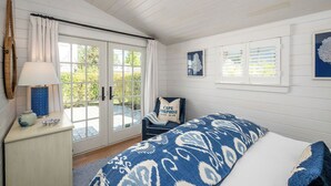 A bedroom with a bed, a chair, a lamp, a window, and a door.