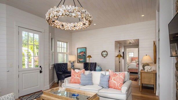 A living room with a white sofa, a coffee table, and a chandelier. There is a door and a window visible.