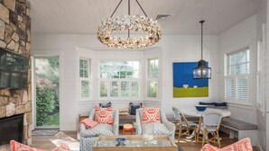 A spacious living room with a stone fireplace, a large chandelier, and a view of the outdoors.