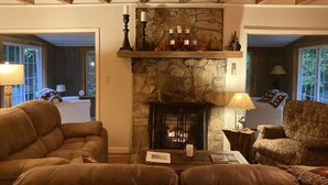 A cozy living room with a stone fireplace, wooden ceiling beams, and comfortable seating.