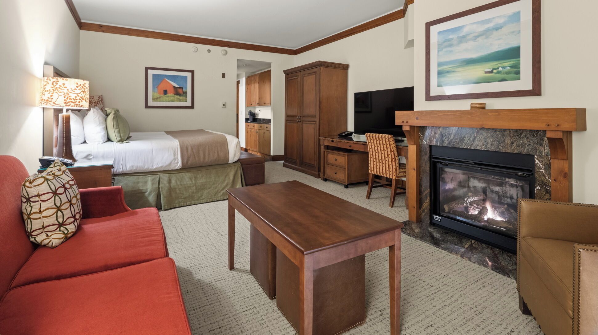 A hotel room with a bed, a sofa, a table, a fireplace, a desk, and a chair.