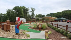 Un campo de mini golf con cerca de madera, un cartel que indica el hoyo 6 y césped artificial verde.