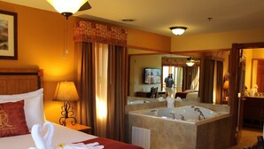 Habitación de hotel con una cama grande, un baño separado con bañera y un espejo que refleja la habitación.
