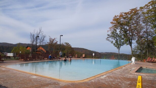 Una piscina con bordeado de baldosas, rodeada de árboles y vistas a colinas.