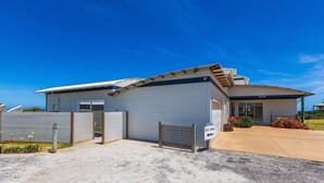 A modern single-story building with a metal exterior, a covered driveway, and a fenced area.