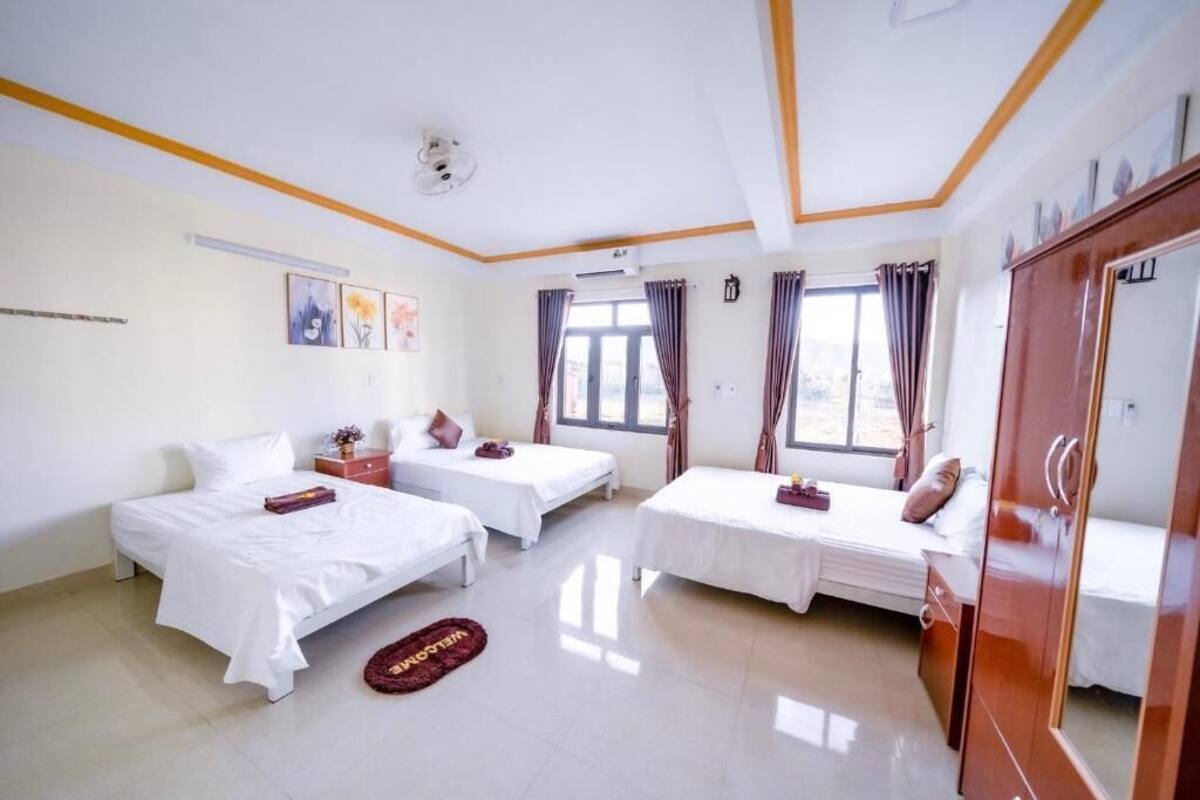 A hotel room with two single beds, a wardrobe, a bedside table, a small rug, and a window with curtains.