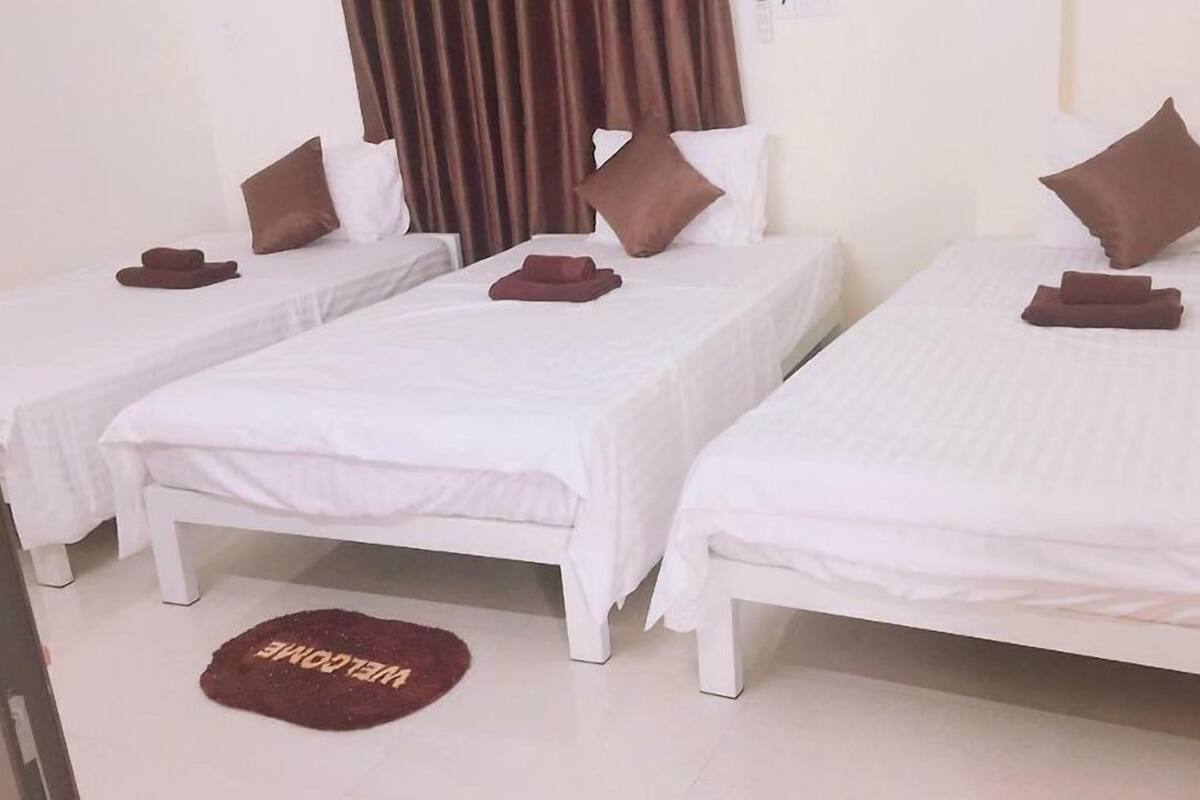 A hotel room with two single beds, each with white bedding and brown pillows, and a welcome mat on the floor.
