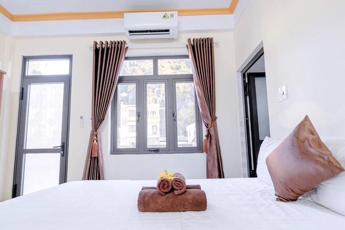 A hotel room with a bed, a window, curtains, and an air conditioning unit.