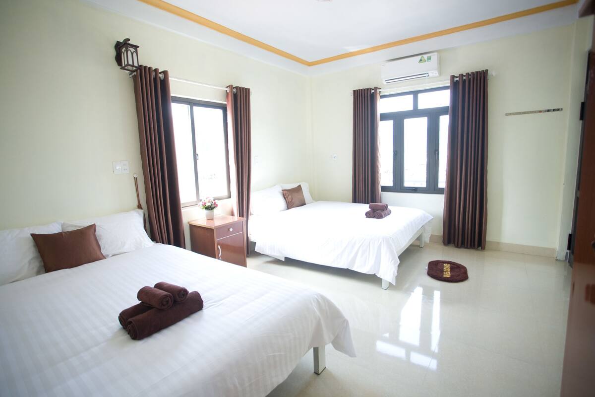A hotel room with two beds, a desk, a window, and an air conditioning unit.