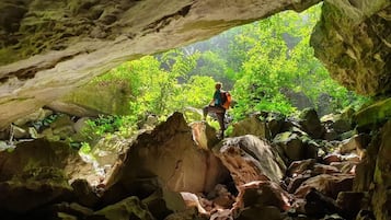 Una persona haciendo senderismo dentro de una cueva, con formaciones rocosas naturales y vegetación en el exterior.