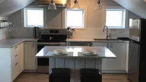 Una cocina moderna con una isla central, dos taburetes de bar, un refrigerador de acero inoxidable e iluminación colgante.