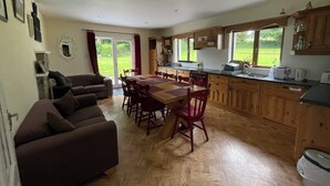 Una cocina amplia con armarios de madera, una mesa de comedor y sillas. Hay una puerta corrediza de vidrio que da a un jardín.