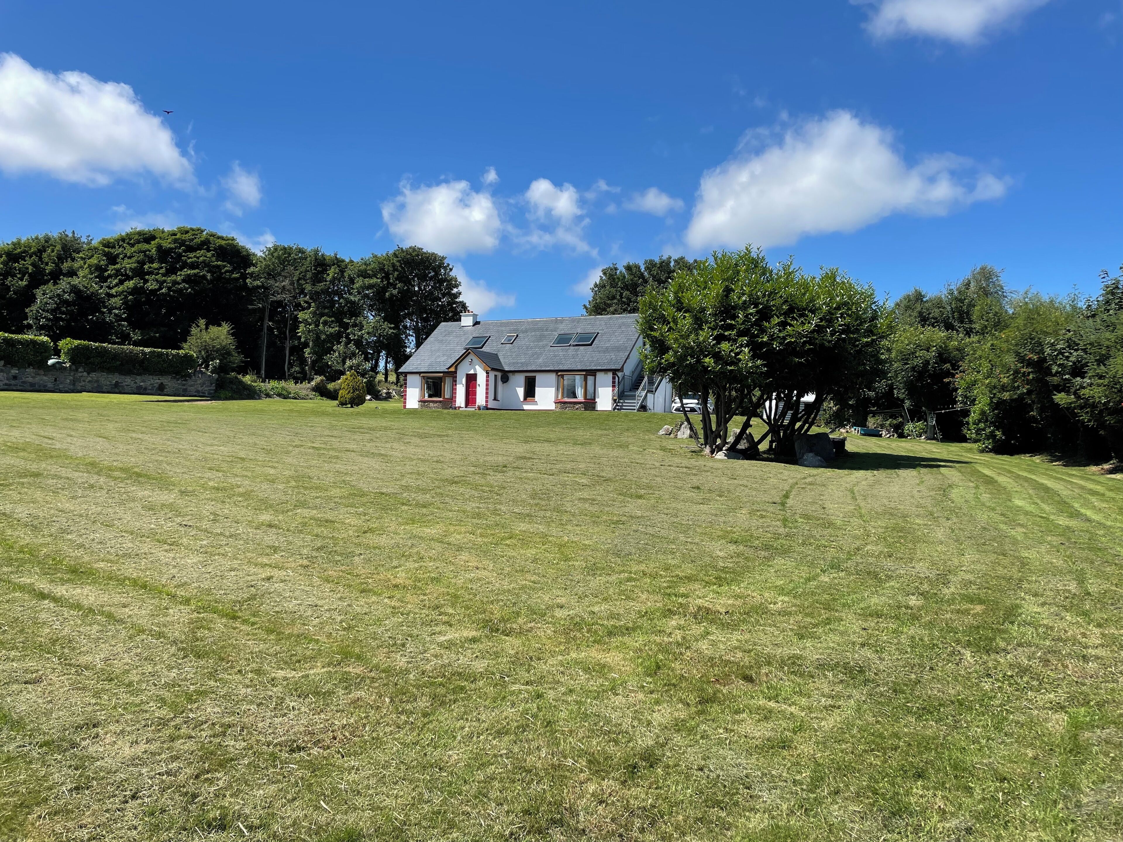 A house with a red door, a grey roof, and a large lawn in front.