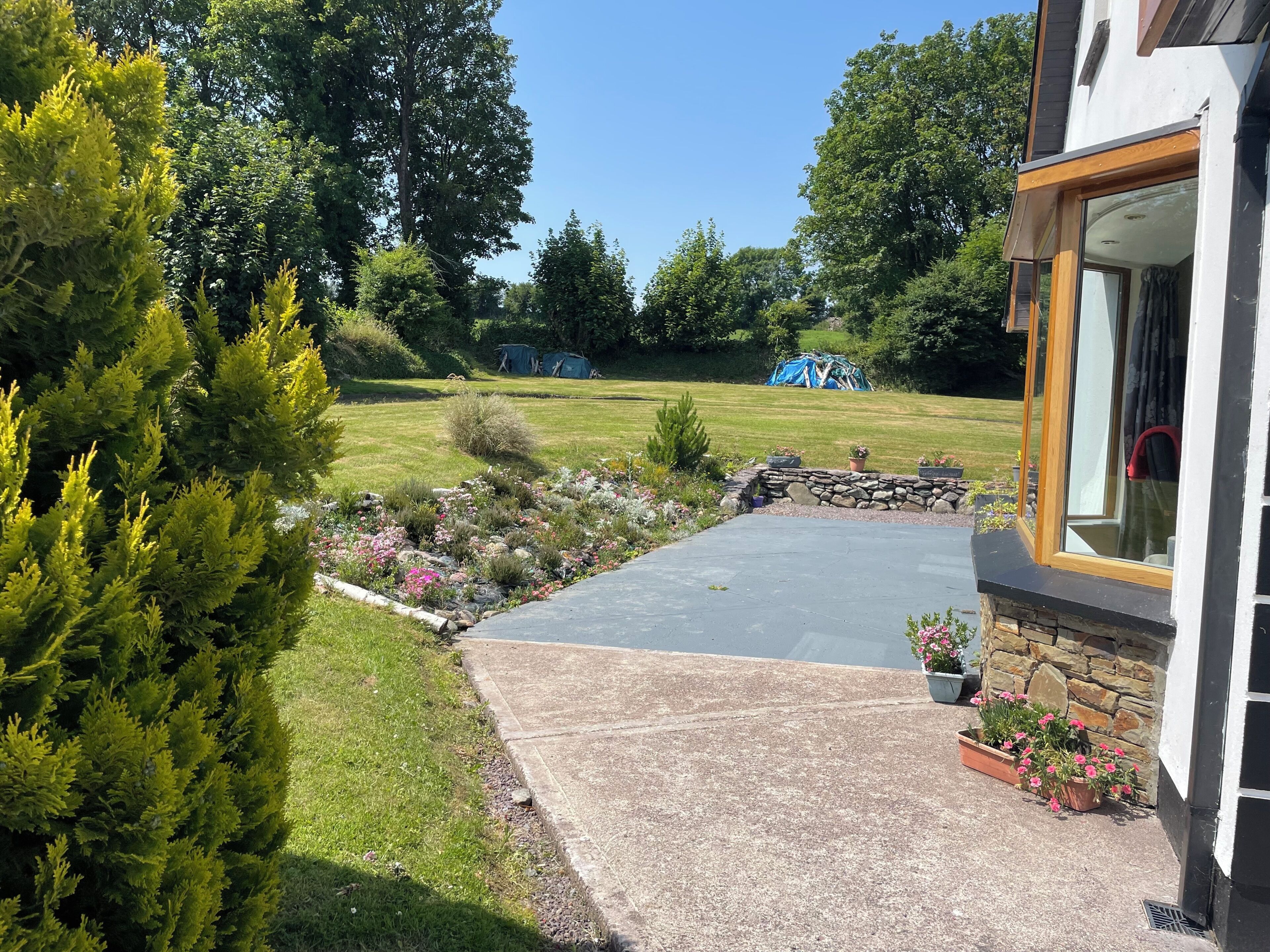 Un giardino residenziale con patio lastricato, muro in pietra e piante in vaso.